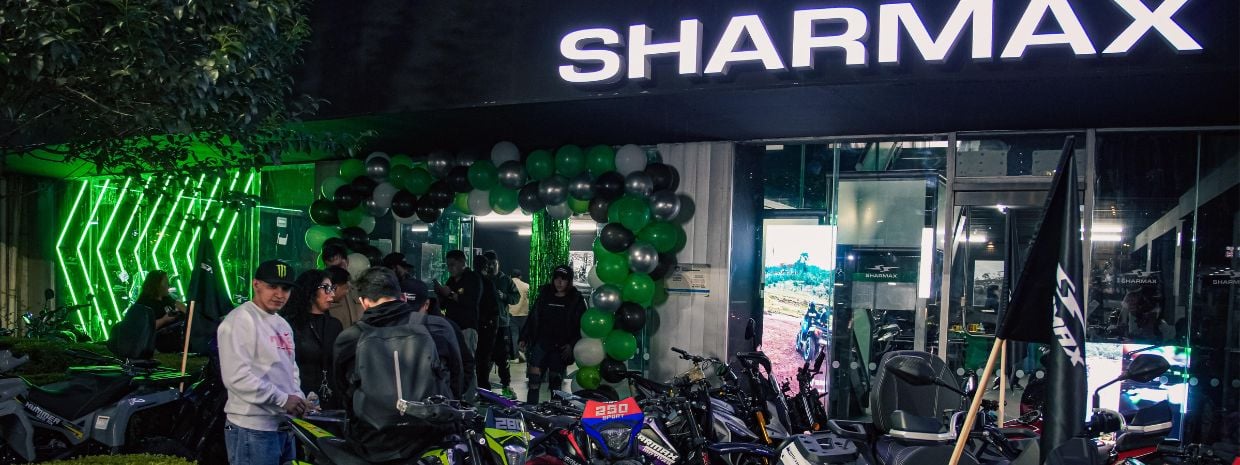 Fachada iluminada de la agencia Sharmax con arco de globos verdes y negros en su evento de inauguración
