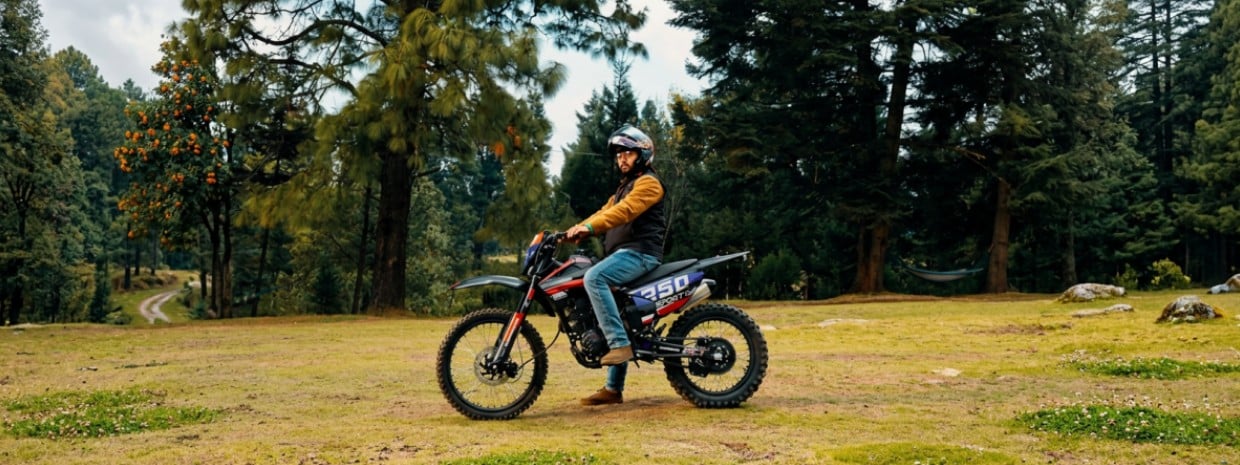 motocicilsta  con casco sobre una Sport 250 en campo con arboles
