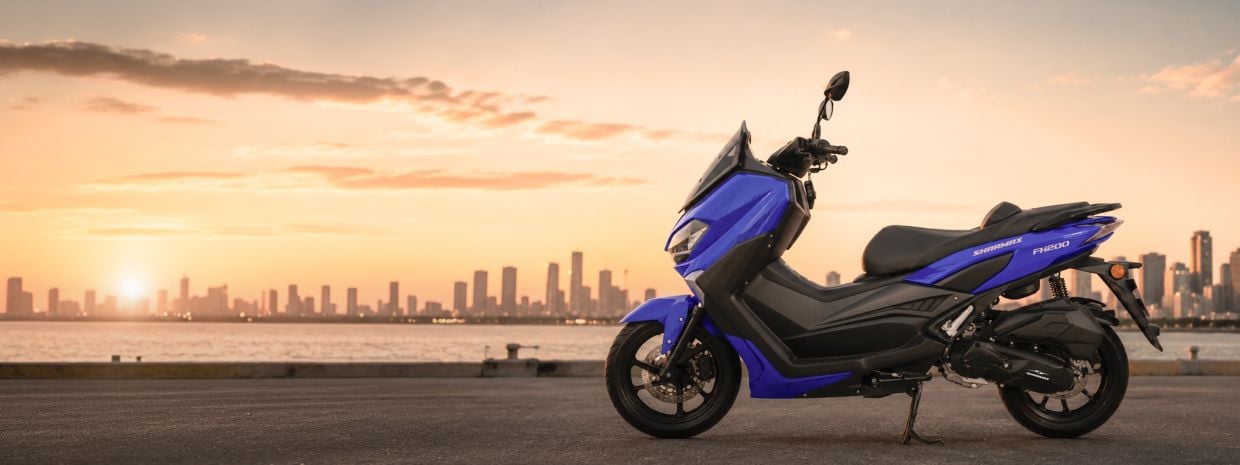 FX 200: compact maxi scooter for the city Blue FX 200 maxi scooter parked on a waterfront at sunset with a city skyline in the background